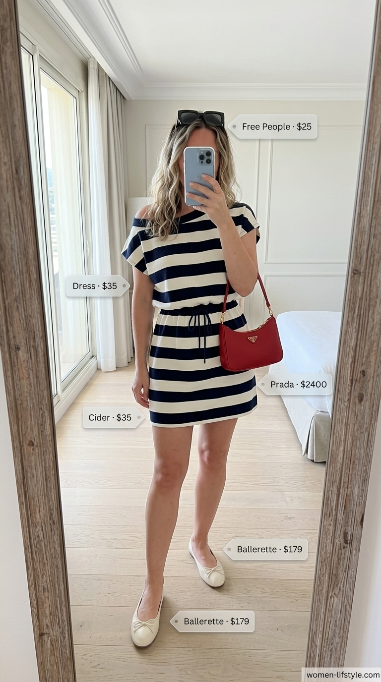 A classic Riviera-inspired mini summer sundress 2026 in navy and white stripes, paired with oversized sunglasses, a white crossbody bag, and red ballet flats for a chic vacation look.